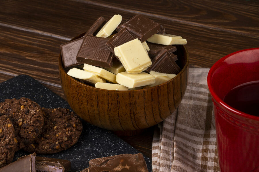 Imagem vista-lateral-de-uma-caneca-com-biscoitos-de-aveia-cha-e-pedacos-de-chocolate-escuros-e-brancos-em-uma-tigela-de-madeira-no-fundo-rustico